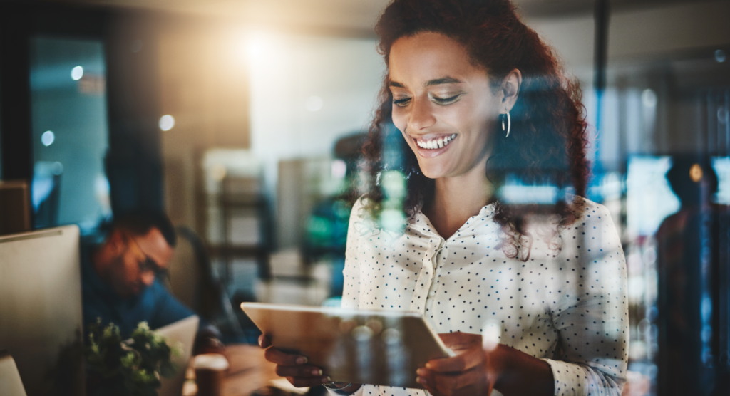 A smiling woman uses a digital tablet in a bright office, symbolizing how clear, in-product storytelling helps users instantly see value and stay engaged.